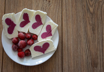 There is a plate with heart-shaped pieces of ice cream on a wooden surface. Ice cream with a pink heart and frozen strawberries are placed on a plate. Top view, flatley.