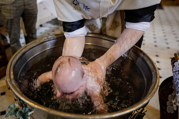 Details with a baby sunk in the baptismal font by an Orthodox priest during the baptism ceremony.