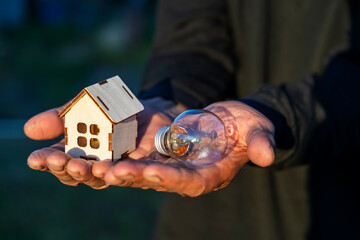 a wooden house and a light bulb in your hands