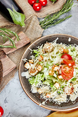 caesar salad on a gray concrete background with burlap bread and tomatoes top view