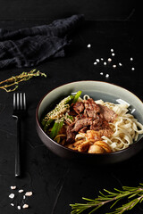 chinese noodles with meat and vegetables in a plate on black texture background