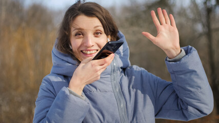 Young student in blue coat is using her smartphone to send a voice message to a new social network...