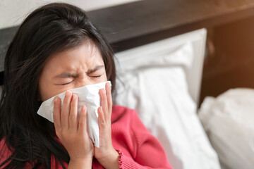 Sick asian girl have hight fever flu and sneezing into tissue on bed in bedroom, Healthcare and prevent the spread infection virus concept, Selective focus.