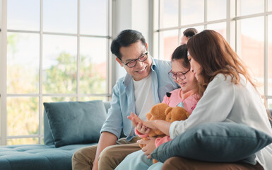 Happy asian family sitting on sofa and playing dolls with their daughter down syndrome child in living room at morning time, Activity happy family lifestyle concept,