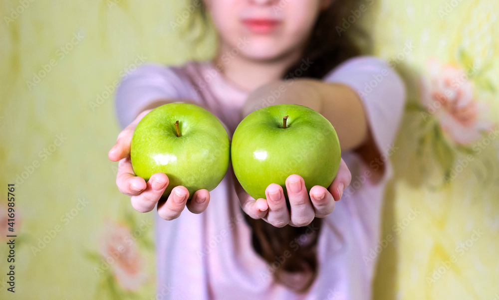 Wall mural the girl holds two green apples in her hands. blurry.