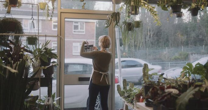 Small business entrepreneur female opening door of plant shop and looking outside for customer