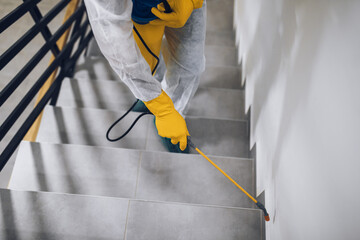 Manual worker in protective work wear spraying virus and bacteria disinfection in residential...