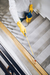 Manual worker in protective work wear spraying virus and bacteria disinfection in residential building with sprayer.