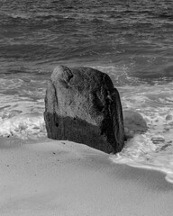 Roca grande en la playa con ola rompiendo sobre ella en blanco y negro