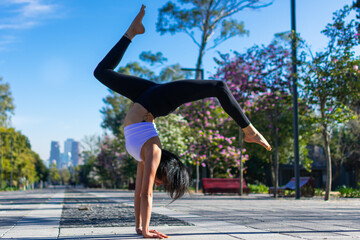 Beautiful sporty fit yogi brunette woman practices yoga in the park handstand asana Bhuja Vrischikasana - handstand scorpion pose