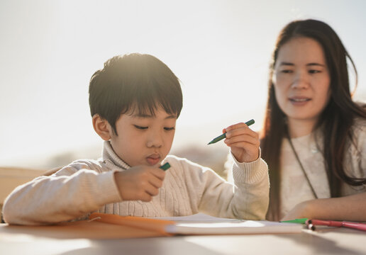 Asian mother doing drawing activities with little son outdoor on patio