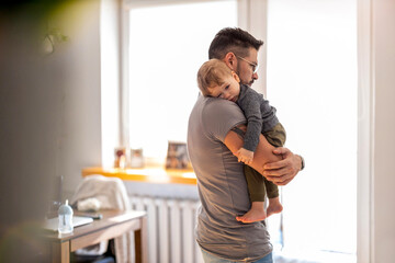 Fototapeta premium Dad putting to sleep baby boy in his arms at home 