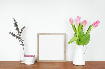 Mock up square wood frame with plant, branches and spring flowers. Wooden shelf against a white wall. Copy space.