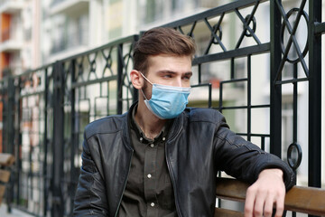 Sad handsome man in medical protective face mask sits on the bench