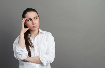 white young woman 20 years old in a white shirt stands thinking on a gray background