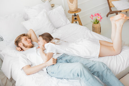 guy and girl lie on a white bed. On the floor are flowers. Flat lay top-down. High angle above top view photo charming lady husband guy couple lying comfortable sheets bed white 