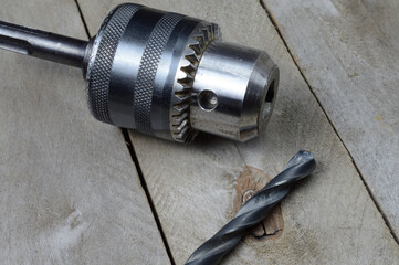 replaceable drill chuck and old drill bits lie on a wooden plank background. close-up.