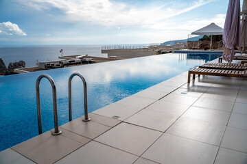 Luxury infinity pool and wooden deck chairs at the resort with beautiful sea views. The concept of recreation, tourism.