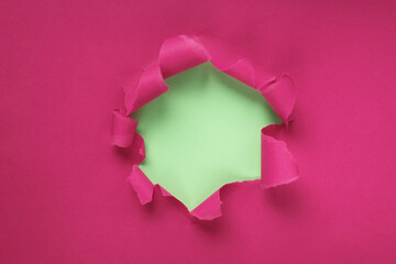 Naklejka na ściany i meble Paper hole with torn sides on a crimson, pink background. Through the paper. A ragged hole.An accurate shot. The concept of advertising and breakthrough. Design for text, print, or advertising content