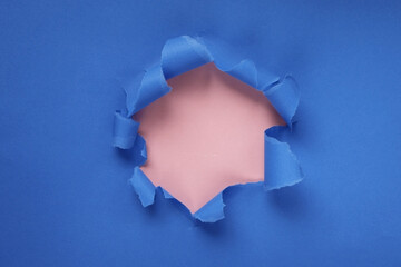 Paper hole with torn sides on a blue-pink background. Through the paper. A ragged hole.An accurate shot. The concept of advertising and breakthrough. Design for text, print, or advertising content.