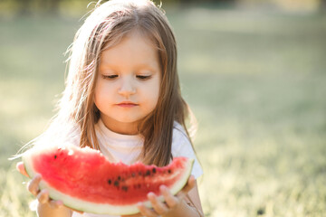 Cute baby girl 3-4 year old eating tasty watermelon over green nature background close up. Healthy lifestyle. Childhood. Summer time.