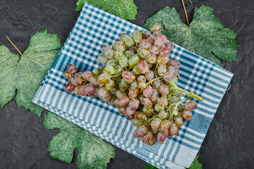 A cluster of red grapes with leaves and blue tablecloth on dark background