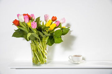 A bouquet of multi-colored tulips in a transparent vase and cup of tea