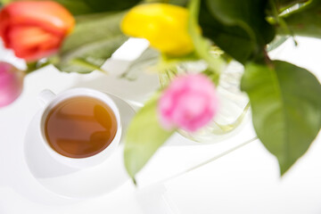 A bouquet of multi-colored tulips in a transparent vase and cup of tea