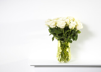 A bouquet of white roses in a vintage green glass vase on a white panel of a fake fireplace.