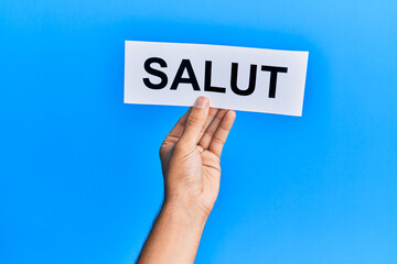 Hand of hispanic man holding salut word paper over isolated blue background.