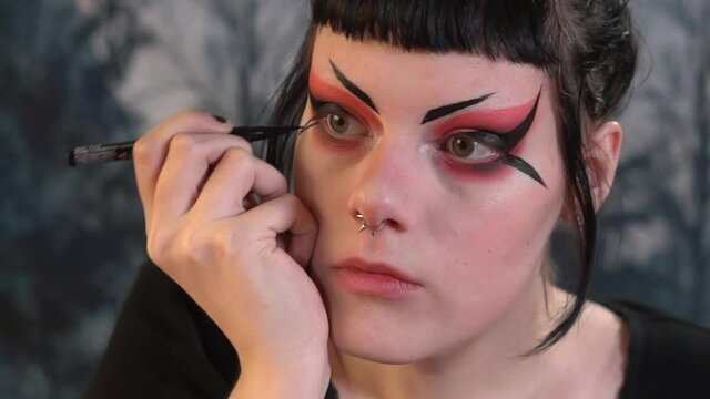 Close up of a teen girl doing elaborate eyeliner for a goth look