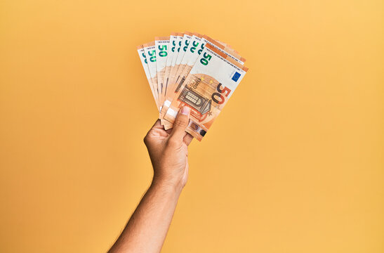 Hand of hispanic man holding 50 euro banknotes over isolated yellow background.