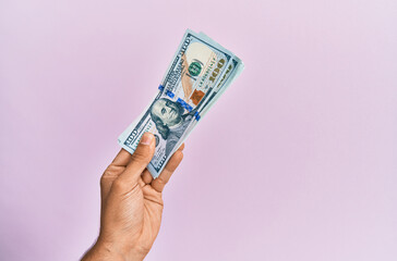 Hispanic hand holding usa dollars banknotes over isolated pink background.