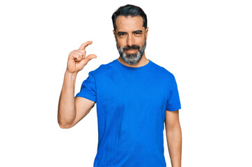 Fototapeta premium Middle aged man with beard wearing casual blue t shirt smiling and confident gesturing with hand doing small size sign with fingers looking and the camera. measure concept.