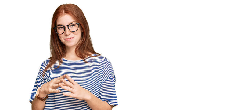 Young read head woman wearing casual clothes and glasses hands together and fingers crossed smiling relaxed and cheerful. success and optimistic