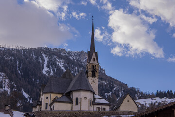 Fototapeta na wymiar Church on a hill in the centre of the city of Moena in the italian dolomites in valley of Fassa on a warm winter day.