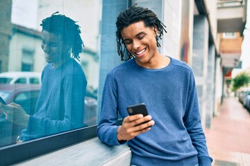 Young african american man smiling happy using smartphone leaning on the wall.