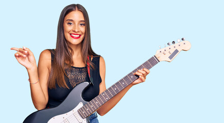Fototapeta premium Young hispanic woman playing electric guitar smiling happy pointing with hand and finger to the side