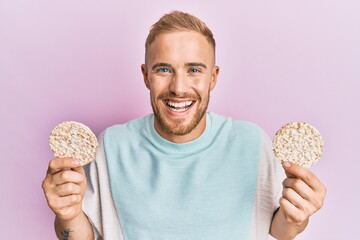 Young caucasian man eating healthy rice crackers smiling and laughing hard out loud because funny...