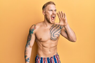 Fototapeta premium Young caucasian man wearing swimwear shirtless shouting and screaming loud to side with hand on mouth. communication concept.