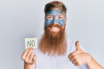 Young irish redhead man wearing facial mask holding no reminder smiling happy and positive, thumb up doing excellent and approval sign