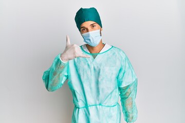Young handsome man wearing surgeon uniform and medical mask smiling doing phone gesture with hand and fingers like talking on the telephone. communicating concepts.