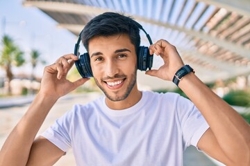 Young latin man smiling happy listening to music using headphones at the city.