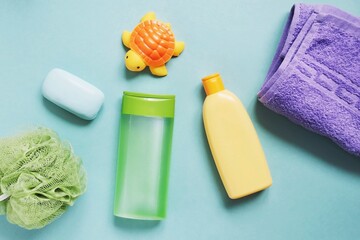 Baby care cosmetic products on a green background. Green sponge, natural shampoo, cleansing gel, soap bar, purple towel and rubber turtle. Object photography, toiletries set