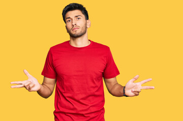 Young handsome man wearing casual red tshirt clueless and confused with open arms, no idea concept.