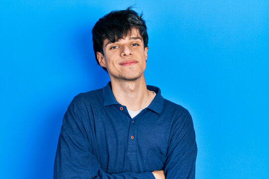 Handsome hipster young man stranding over blue background happy face smiling with crossed arms looking at the camera. positive person.