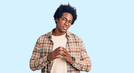 Handsome african american man with afro hair wearing casual clothes and glasses hands together and fingers crossed smiling relaxed and cheerful. success and optimistic