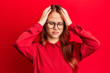 Young beautiful redhead woman wearing casual clothes and glasses over red background suffering from headache desperate and stressed because pain and migraine. hands on head.