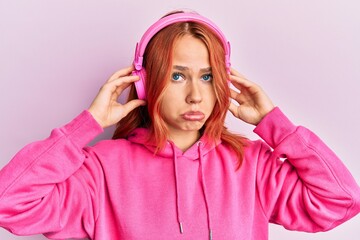 Young redhead woman listening to music using headphones depressed and worry for distress, crying angry and afraid. sad expression.