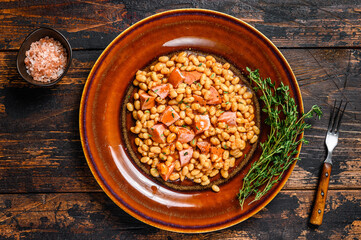 Kidney beans with smoked sausage and tomato sauce in a plate. Dark wooden background. Top view